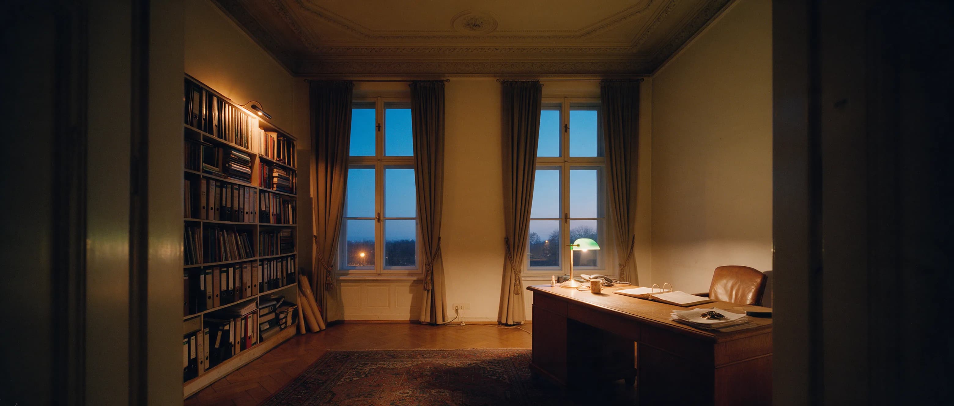 Schreibtisch am hohen Fenster eines Leipziger Altbaubüros zur blauen Stunde